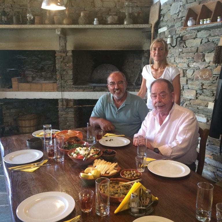 two men sitting at the table with various aperitifs and a woman behind them and watching at the camera at 'Narlis Farm'